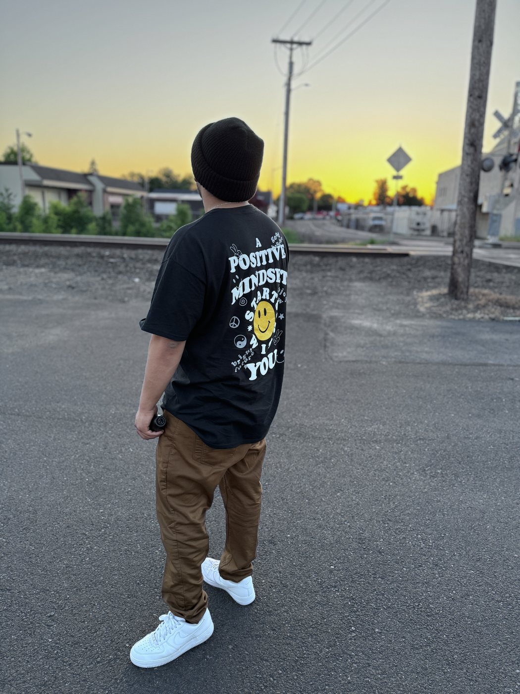 Belinskii at a railroad crossing at sunset in a Positive Mindset tee
